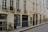 A quiet street with beige-colored residential buildings featuring multiple windows adorned with decorative wrought iron railings and potted plants. A small sign for 'Jean de Beauvais' is visible, adding a touch of character. The buildings exhibit classic urban architecture with subtle weathering.