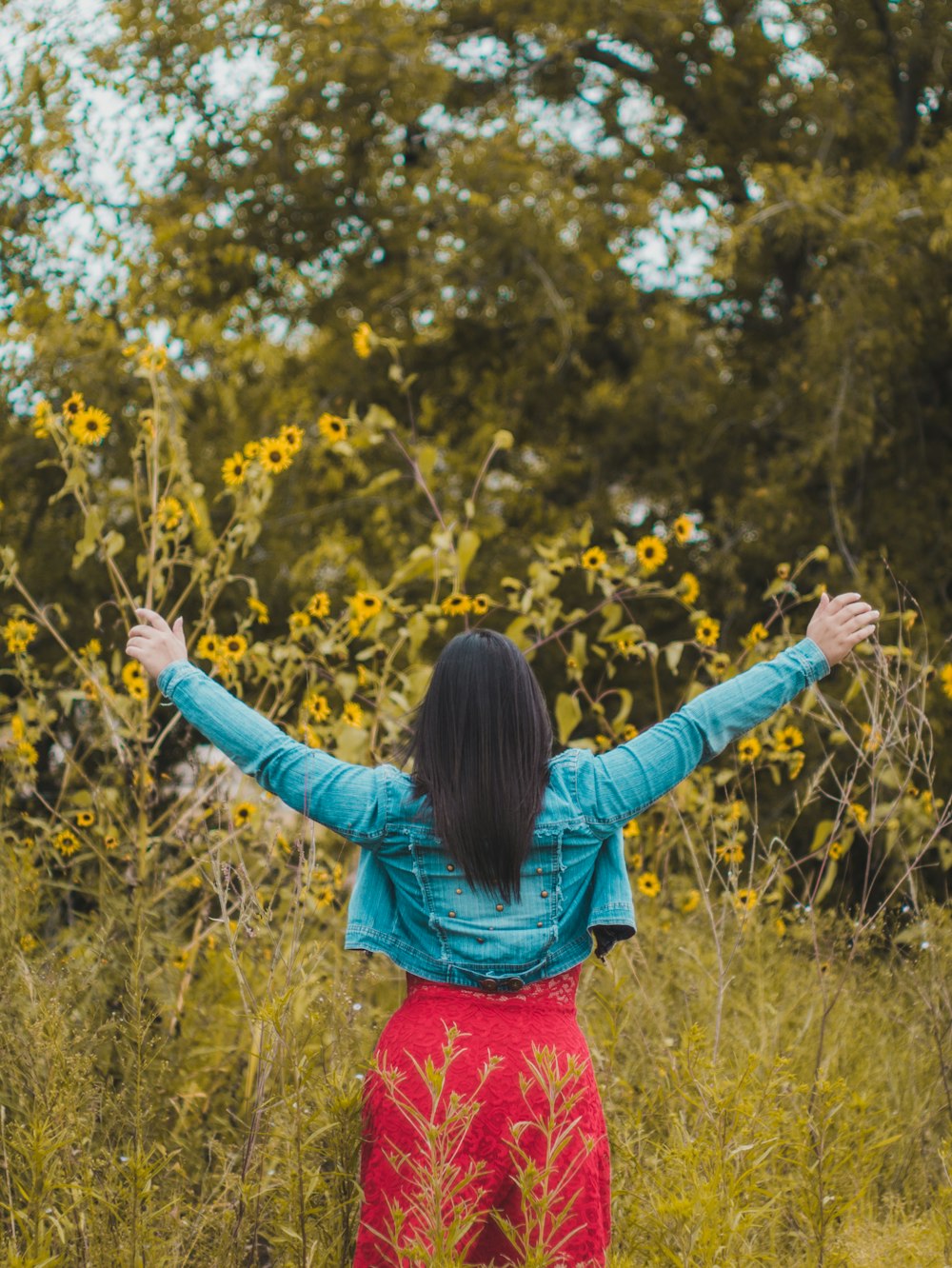 woman raising two hands in front of yellow sunflowers