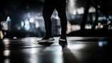 Dynamic photo of feet walking on asphalt with blurred city lights in the background, capturing motion.