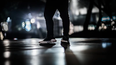 Dynamic photo of feet walking on asphalt with blurred city lights in the background, capturing motion.