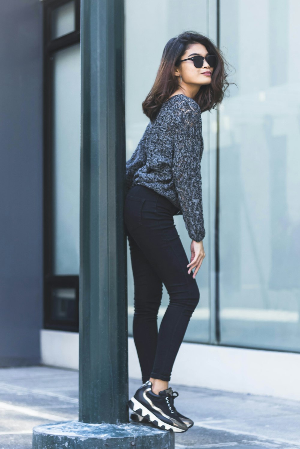 woman in gray long-sleeved top and black pants leaning butt on post