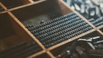 Close-up of hands arranging letters on a typesetting tray in a warm-lit workshop.