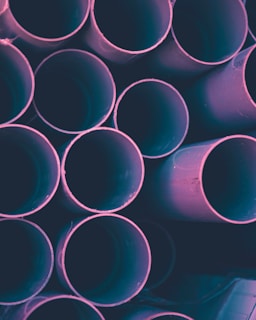 A close-up of sturdy boring pipes stacked neatly in a rural warehouse under soft sunlight.