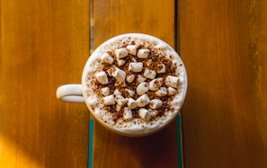 Rich dark cocoa powder being sprinkled over a warm cup of cocoa drink in a cozy setting
