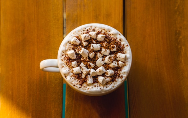 A tall glass of hot chocolate topped with whipped cream and a sprinkle of cinnamon, glowing warmly.