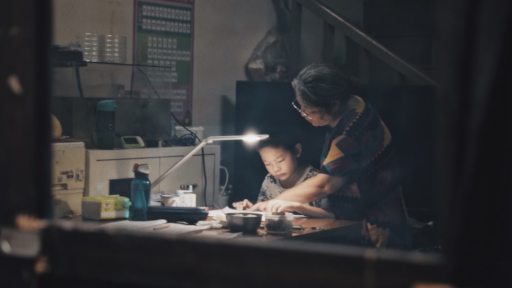 woman standing beside boy sitting front of table