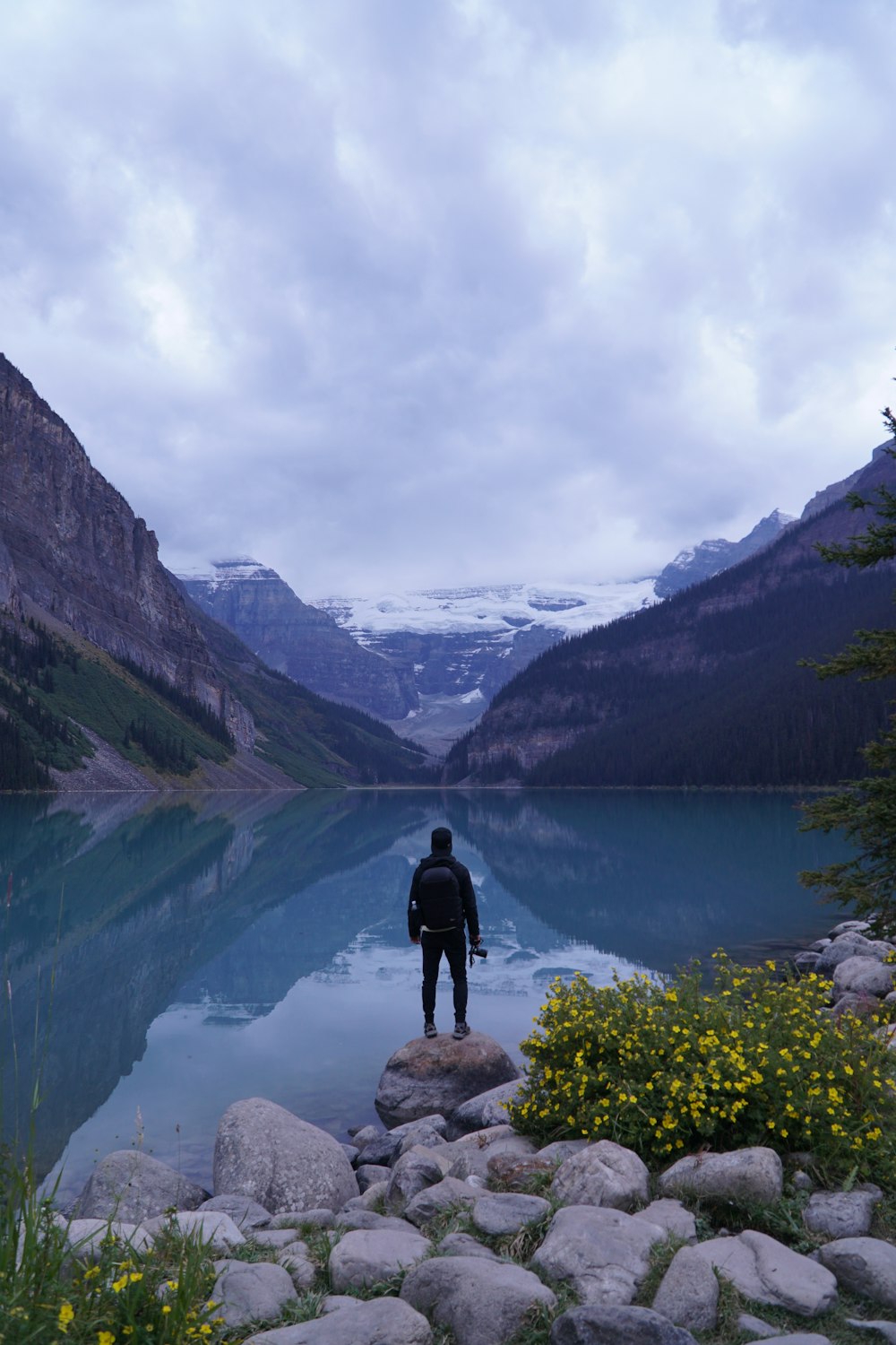 man standing on rock facing the body of water