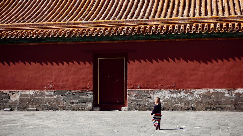 toddler walking straight in front of red painted building