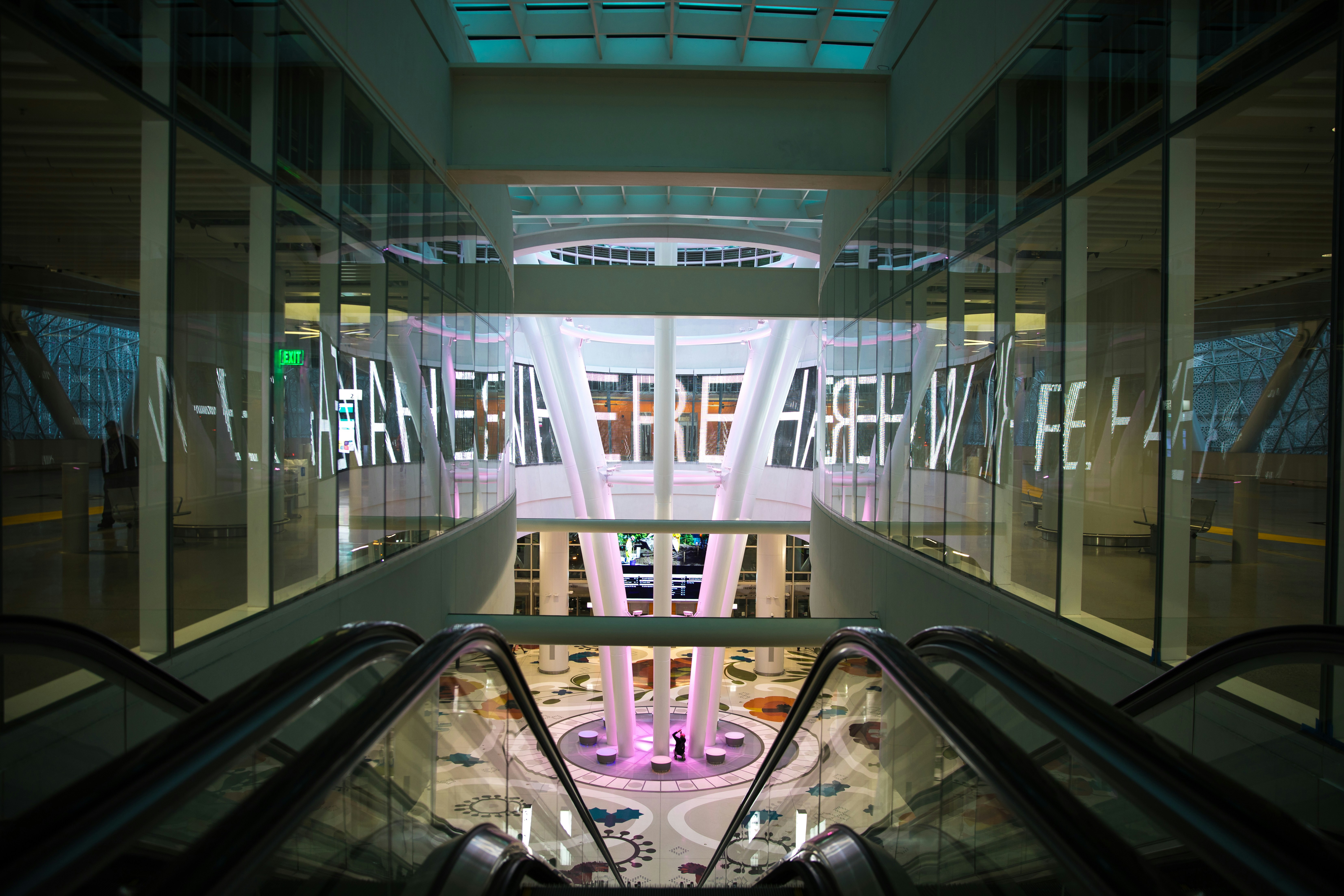 an escalator in a large building with a neon sign above it