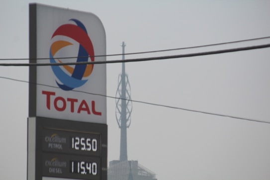 A tall sign for Total with the company's logo and current petrol and diesel prices. The backdrop includes an overcast sky and visible power lines overhead.