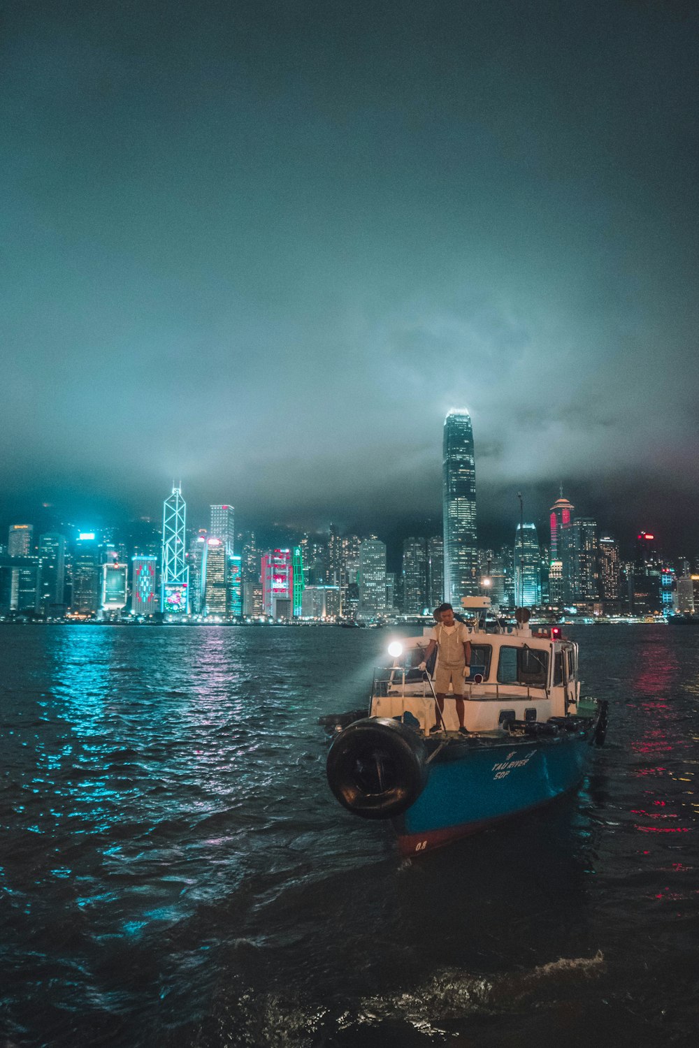 person standing on fishing boat near buildings at night