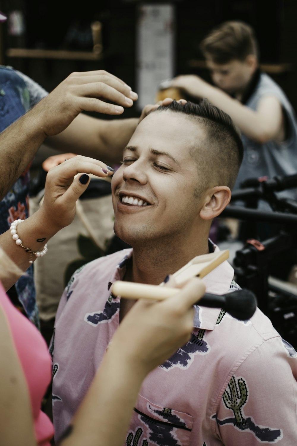 two people putting makeup on man's face