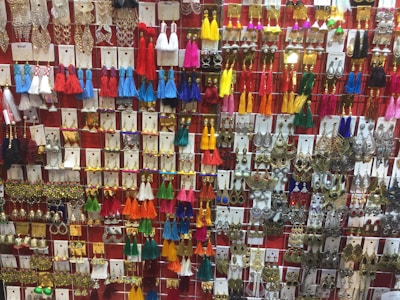 A vibrant display of a wide variety of earrings arranged on a wall, featuring tassels, metallic designs, and colorful beads. The earrings are organized in neat rows, showcasing an array of designs from traditional to modern styles.