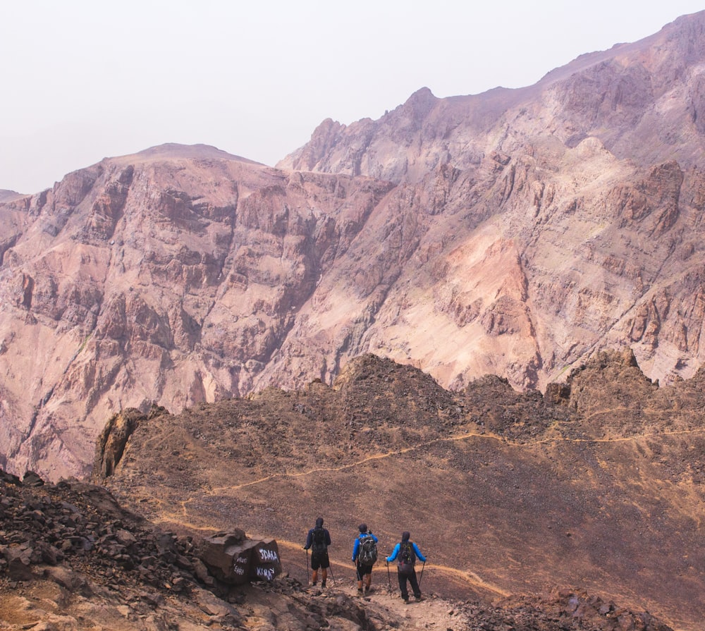 three person standing near mountain