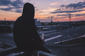 man sitting on handrail front of highway during golden hour