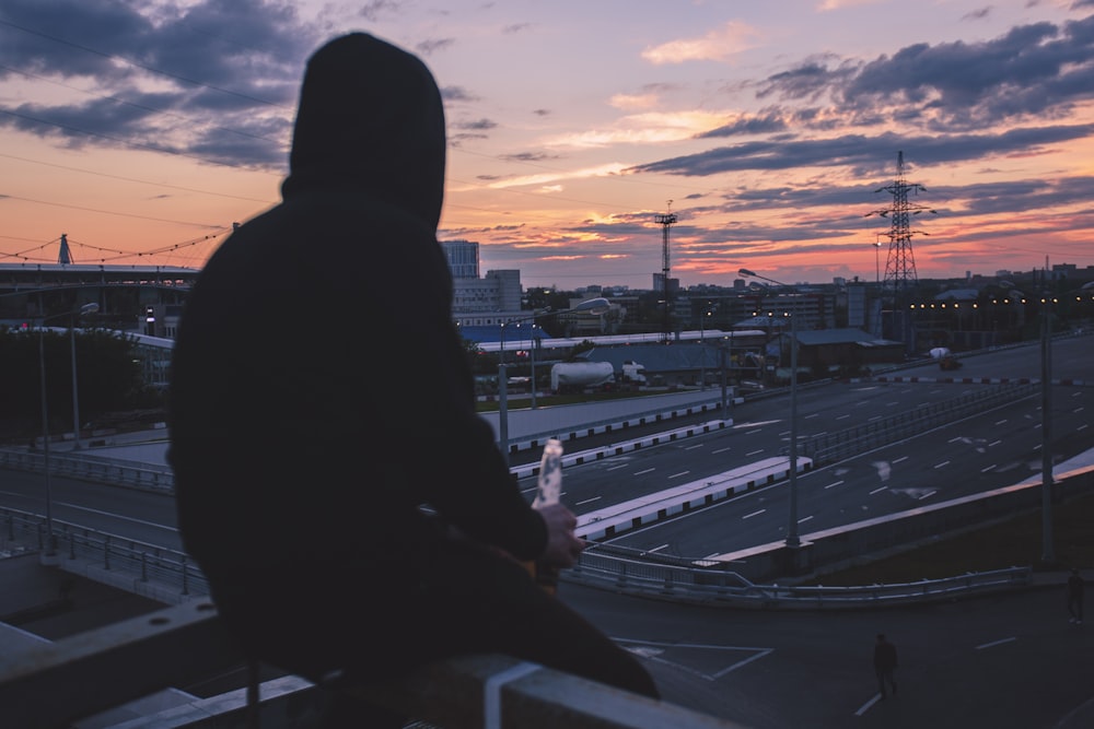 man sitting on handrail front of highway during golden hour