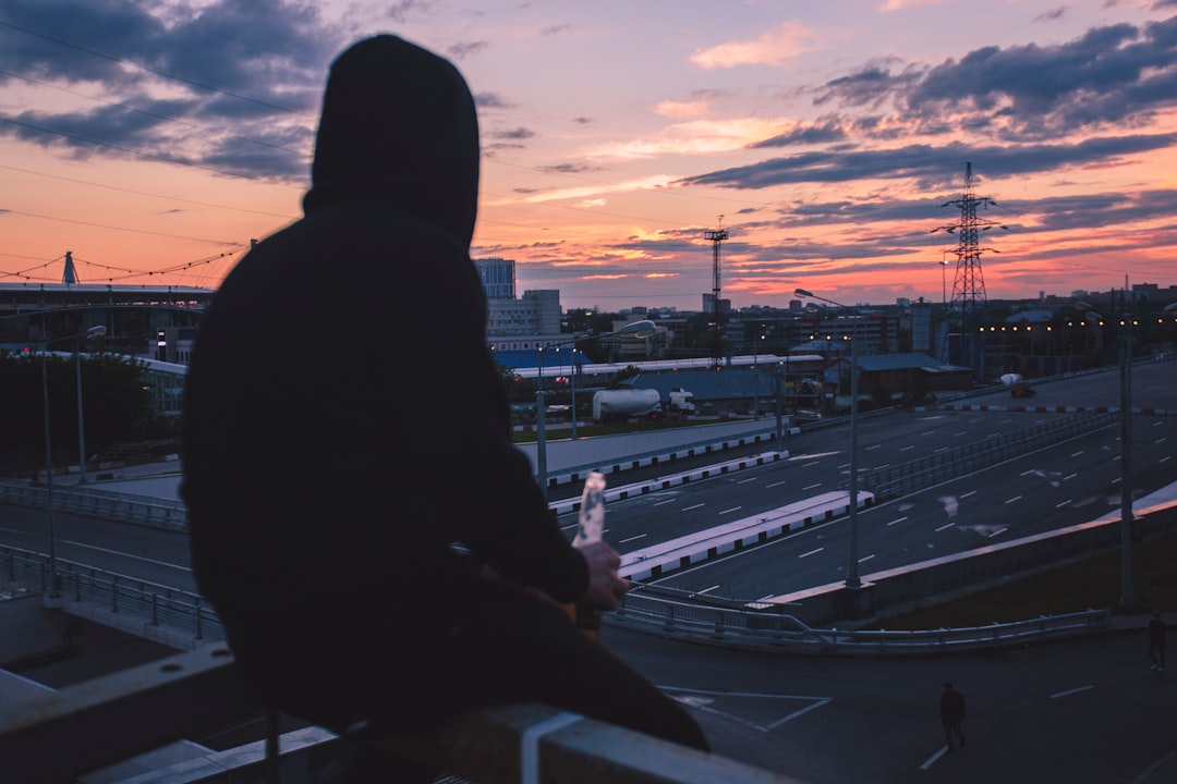 man sitting on handrail front of highway during golden hour