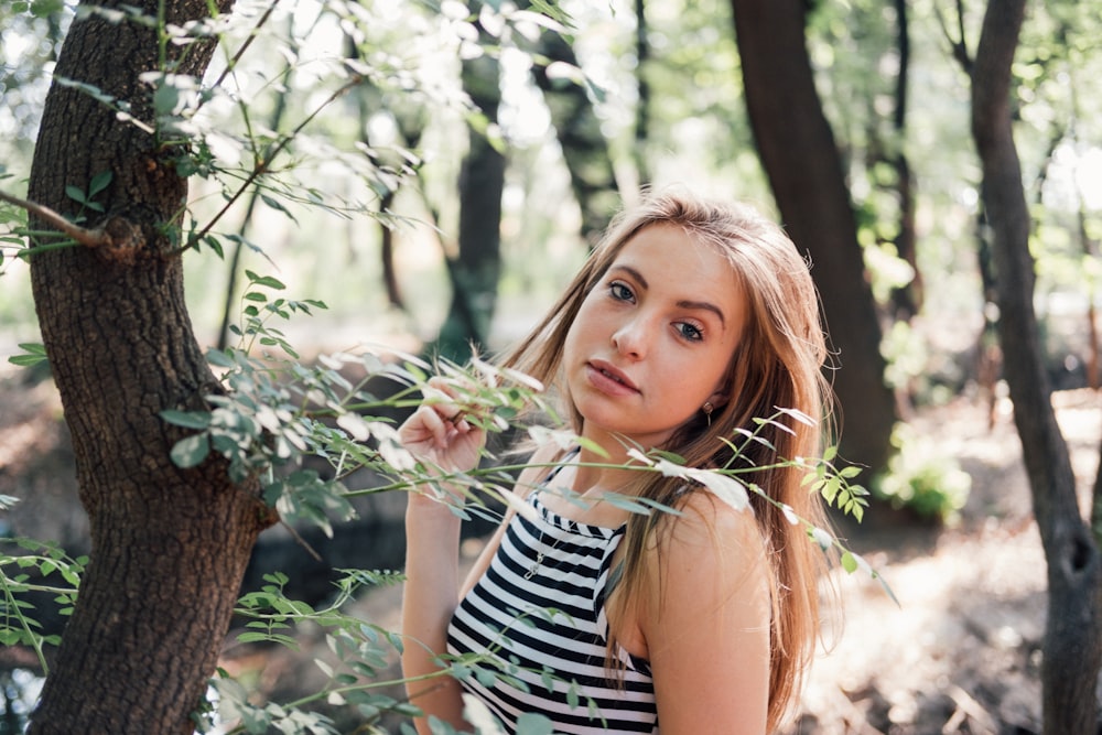 woman in black and white striped top standing beside tree