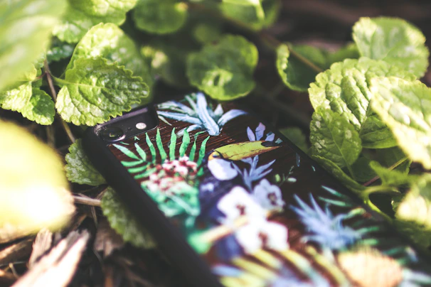A soothing phone case featuring delicate forest leaves in off-white and light cyan tones resting on a wooden table.