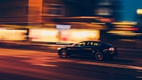 Dynamic shot of a modified street car tearing through an urban night scene with blurred city lights.