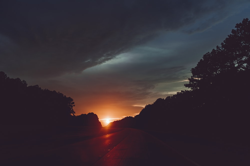 the sun is setting behind the trees on the side of the road