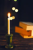 Warmly glowing candles placed on a wooden table beside a stack of educational books.