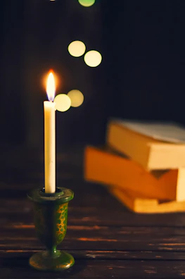 Warmly glowing candles placed on a wooden table beside a stack of educational books.