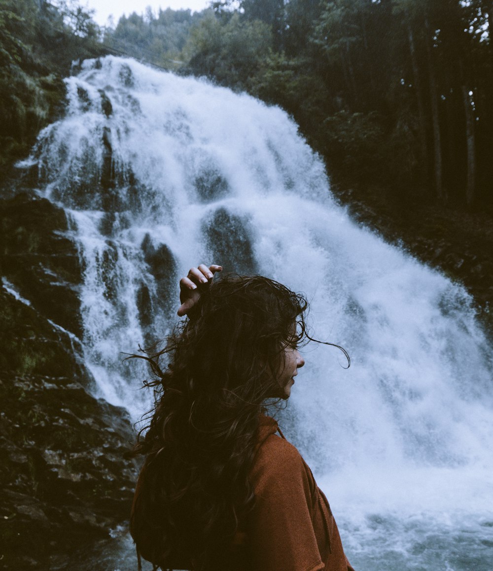 woman in brown shirt near waterfalls at daytime