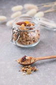 Clear glass jar filled with crunchy homemade granola topped with nuts and dried fruits on a linen cloth.