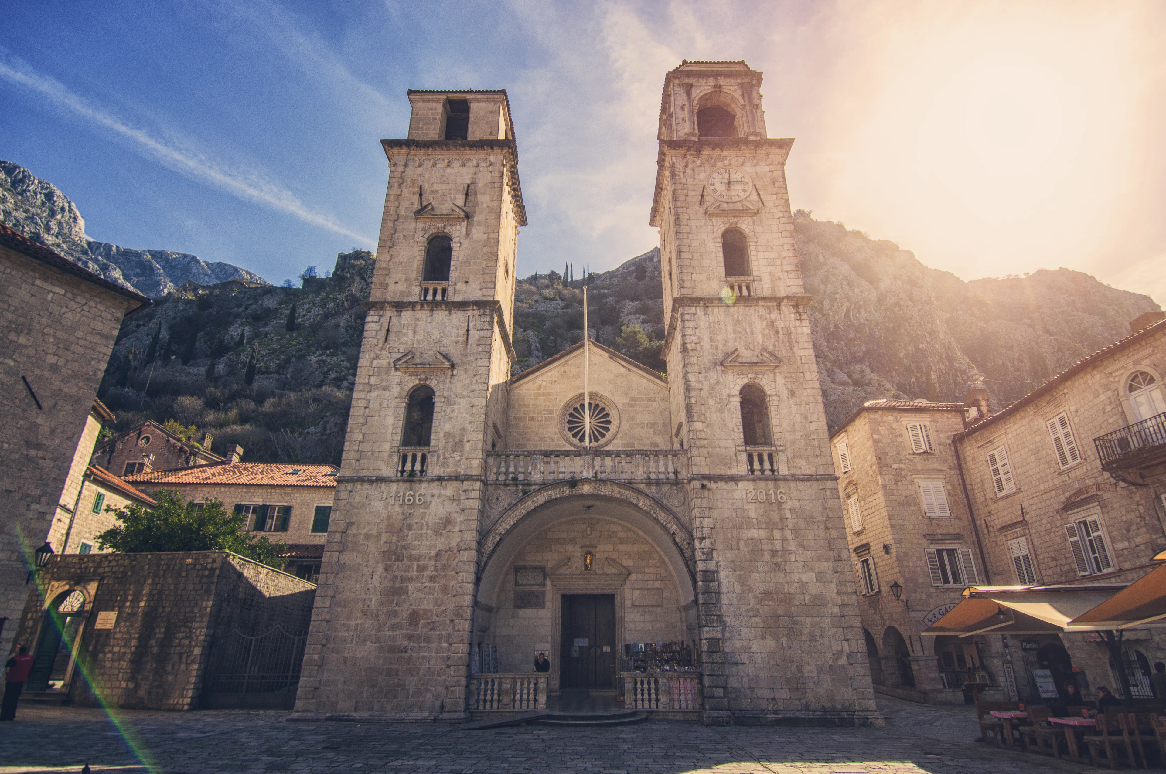 The two stone bell towers of St. Tryphon's Cathedral in Kotor's old town, bare mountain rock rising behind