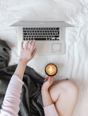 A person working on a laptop at a cozy home desk with a cup of coffee nearby.
