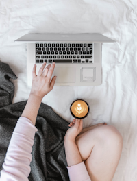 A student comfortably learning on a laptop at home with a cup of coffee nearby.