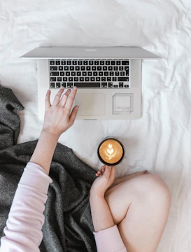 A person working on a laptop at a cozy home desk with coffee.
