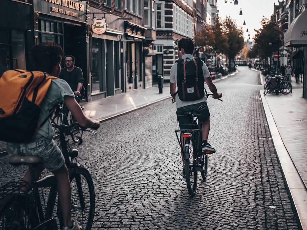 duas pessoas andando de bicicleta na rua perto de edifícios