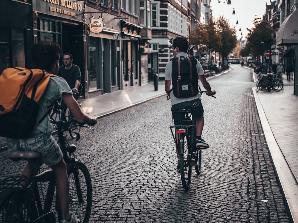 two person riding bicycle on street near buildings