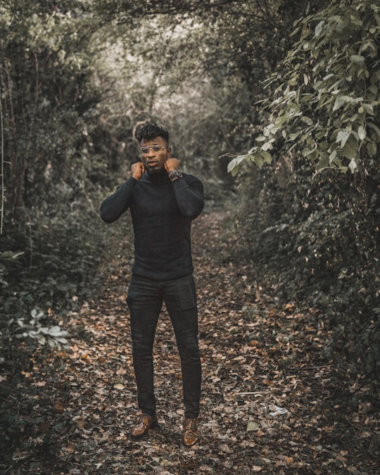 standing man wearing black turtleneck sweater and black fitted pants surrounded with trees during daytime in Milton Keynes United Kingdom