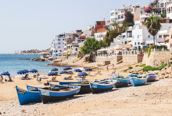 Fishing boats and parasols on the beach below the village — Taghazout, Morocco