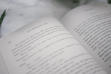 An open book on a flat surface shows text on two facing pages. The visible page on the left is numbered 158 and contains a reference to 'Lisa Brennan-Jobs.' The text appears to be a narrative, possibly non-fiction or a memoir excerpt.
