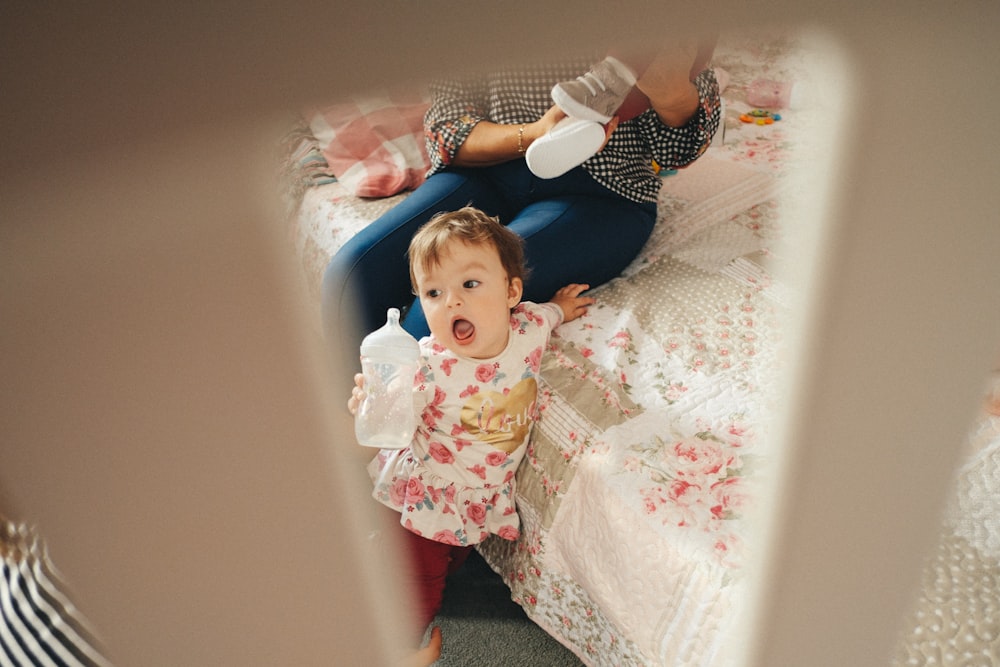 baby holding nursing bottle while standing near bed