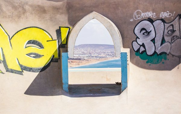 A graffitied arch framing the sea — Taghazout, Morocco