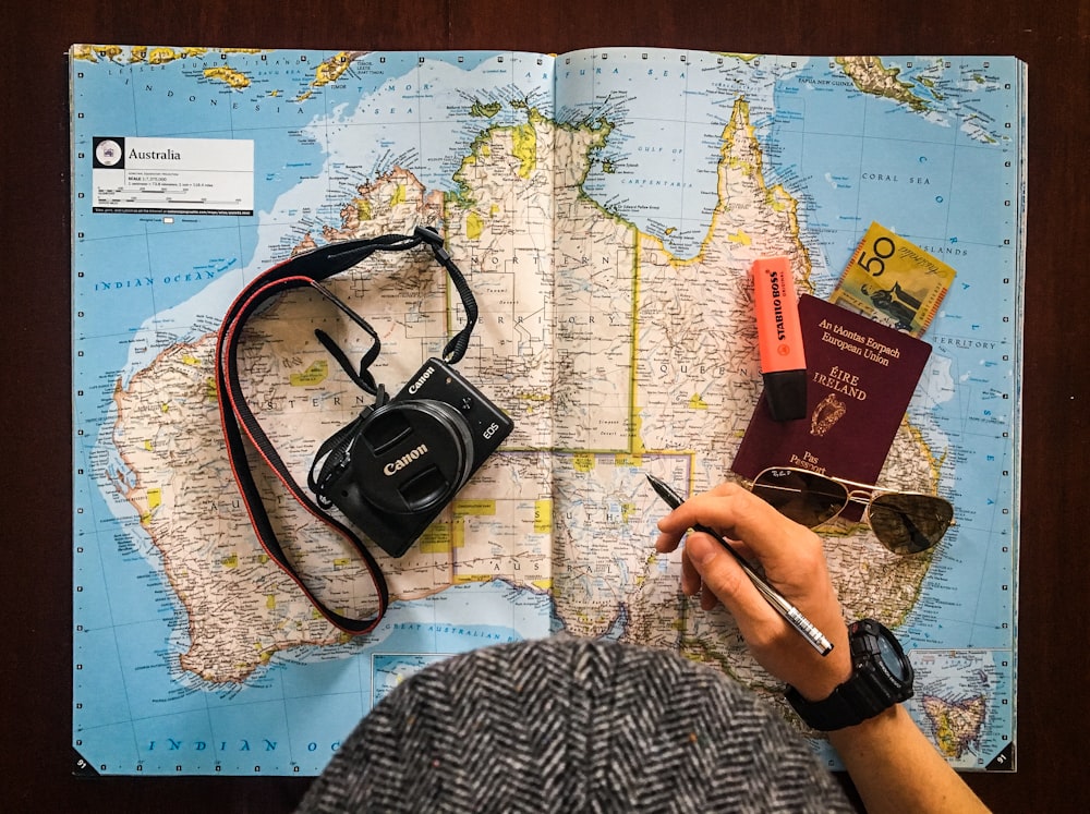 flat lay photography of person holding pen in front of world map