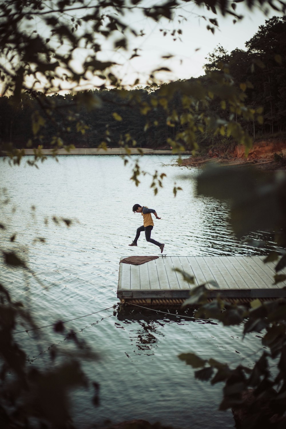 man jumping on wooden dock above body of water