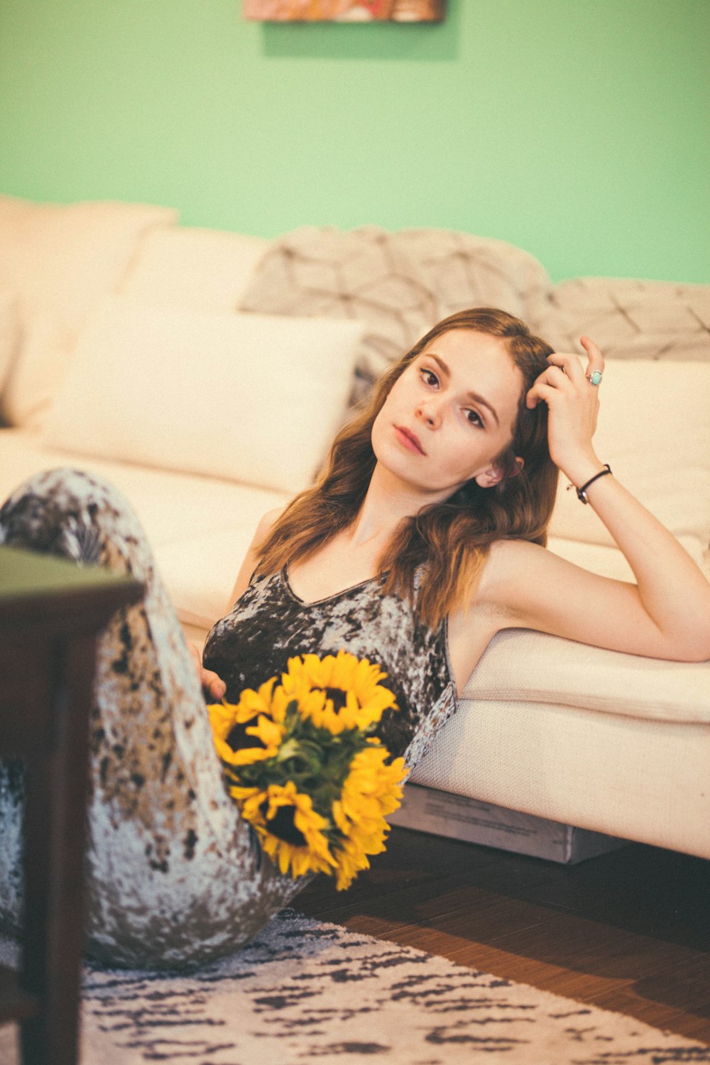woman wearing grey and black tank top sitting on floor leaning on sofa while holding yellow sunflower