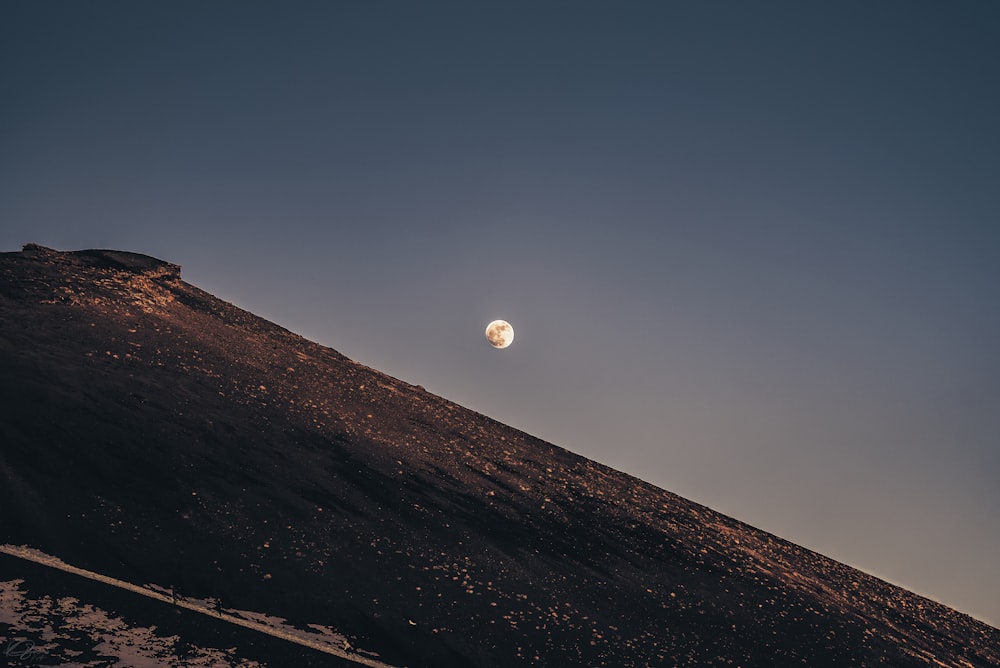 uma lua cheia nascendo sobre uma colina no deserto