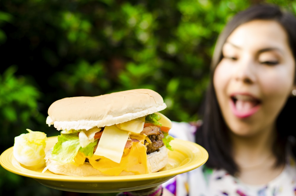 selective focus photo of woman holding plate of sandwich