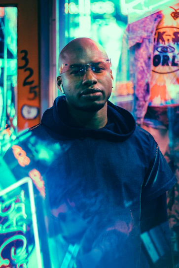 Futuristic man standing confidently with blue and red neon lights in a dark urban environment.