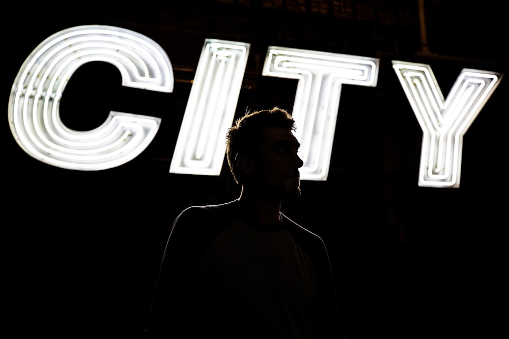Mann steht vor CITY-Lichtbeschilderung