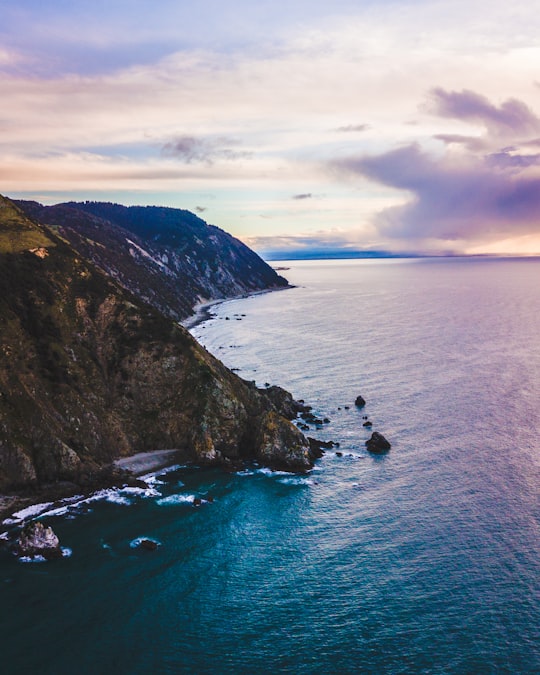 calm body of water crashing on shore of cliff under white clouds in Cable Bay New Zealand