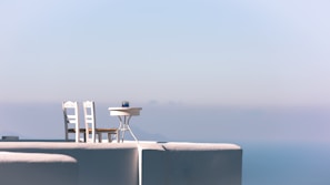 Outdoor patio with white furniture overlooking a calm sea under a clear blue sky
