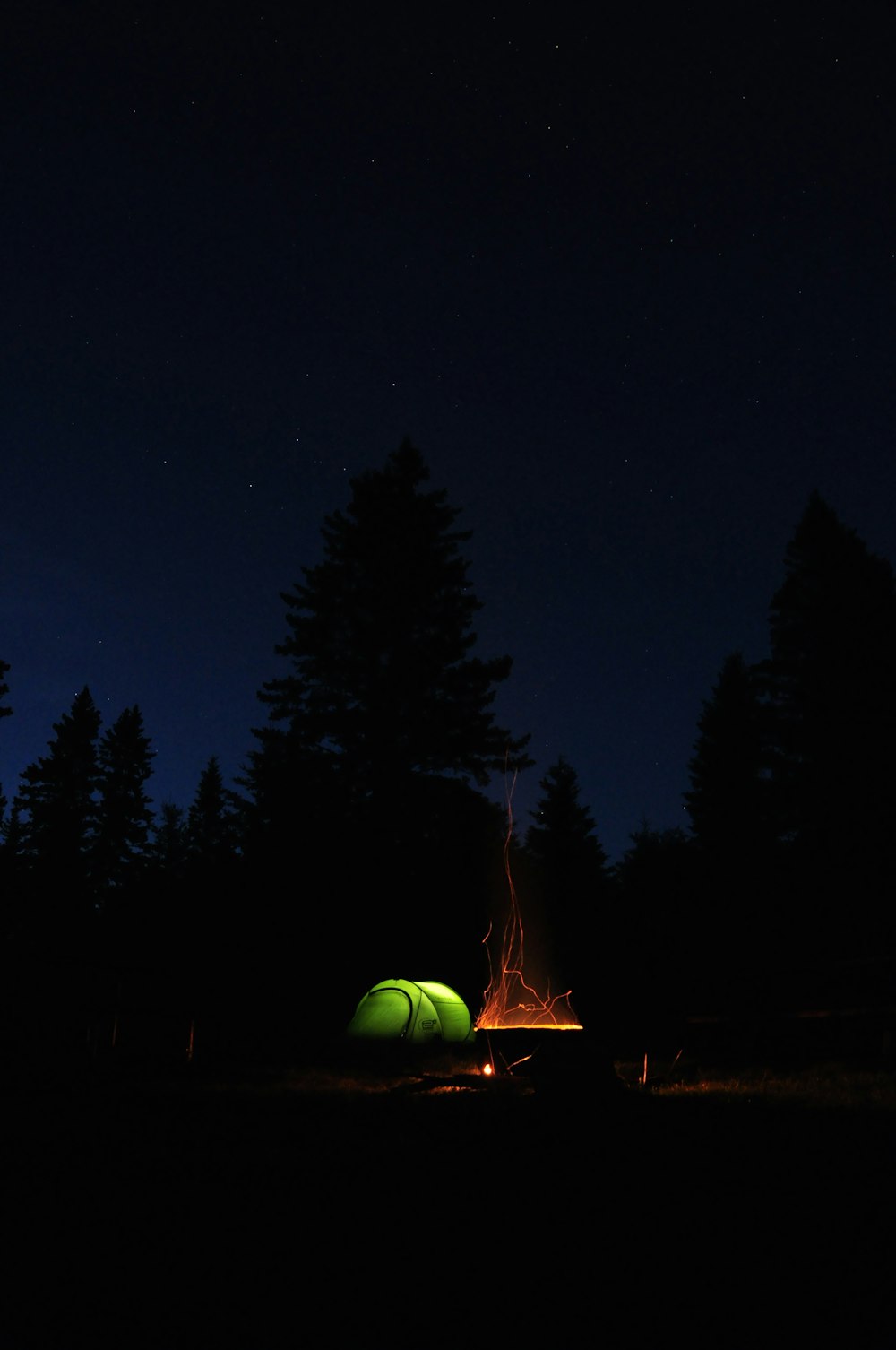 lighted bonfire beside tent at night